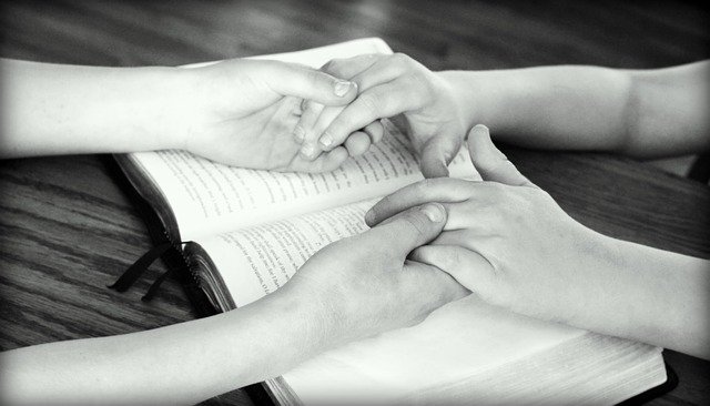 holding hands over Bible praying